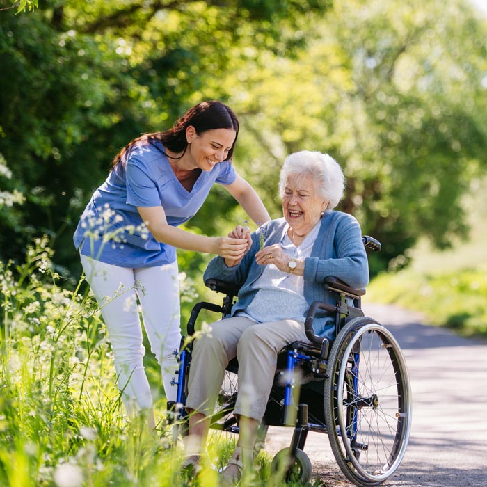 caretaker walking with elderly woman in wheelchair