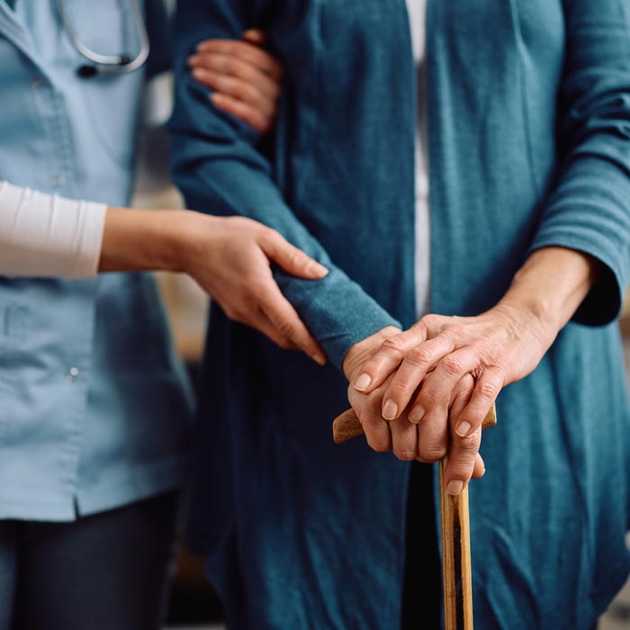 caretaker helping elderly woman with cane
